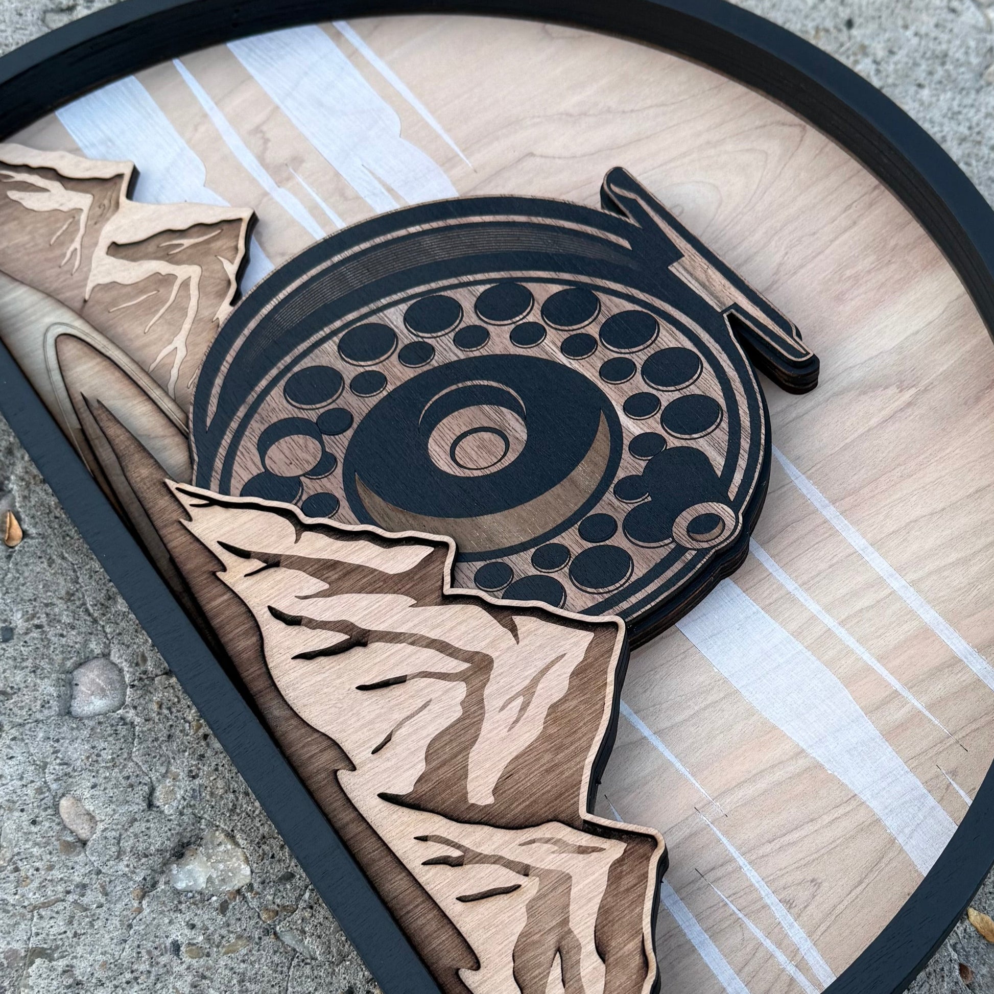 Wooden cutout of a fish and fly fishing reel on a concrete surface