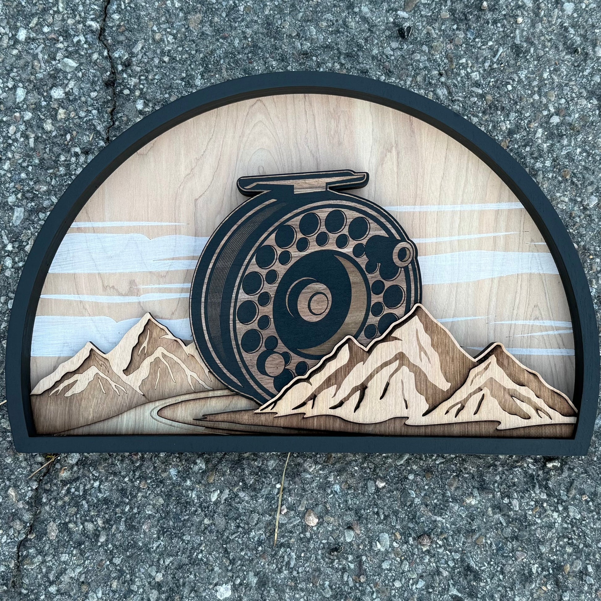 Wooden plaque with fly fishing reel design on a concrete surface